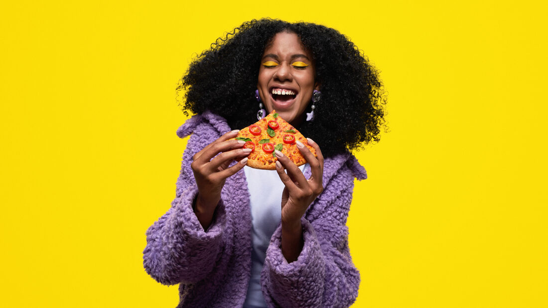 Mujer disfrutando pizza sobre fondo amarillo